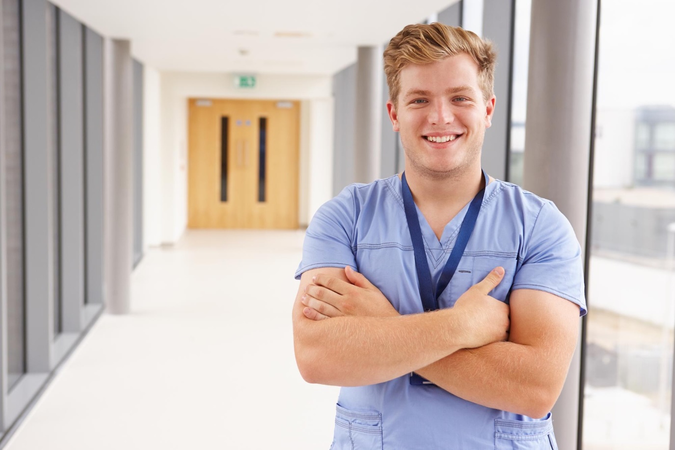Smiling male nurse standing in glass hallway