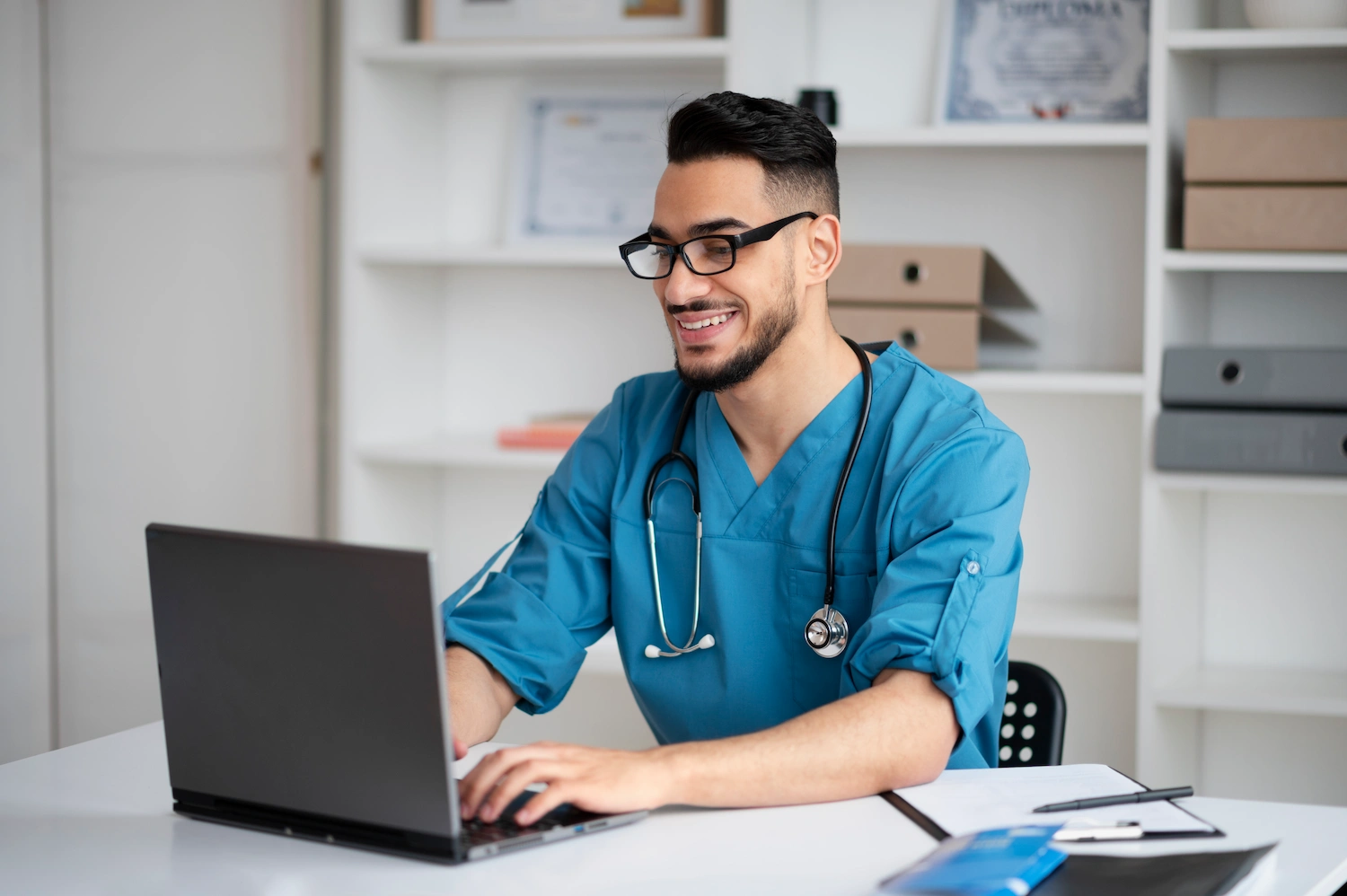 Smiling male clinician writing a travel healthcare resume on a laptop.