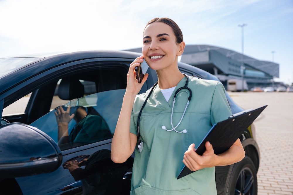 Female travel clinician taking a phone call while standing by her car.