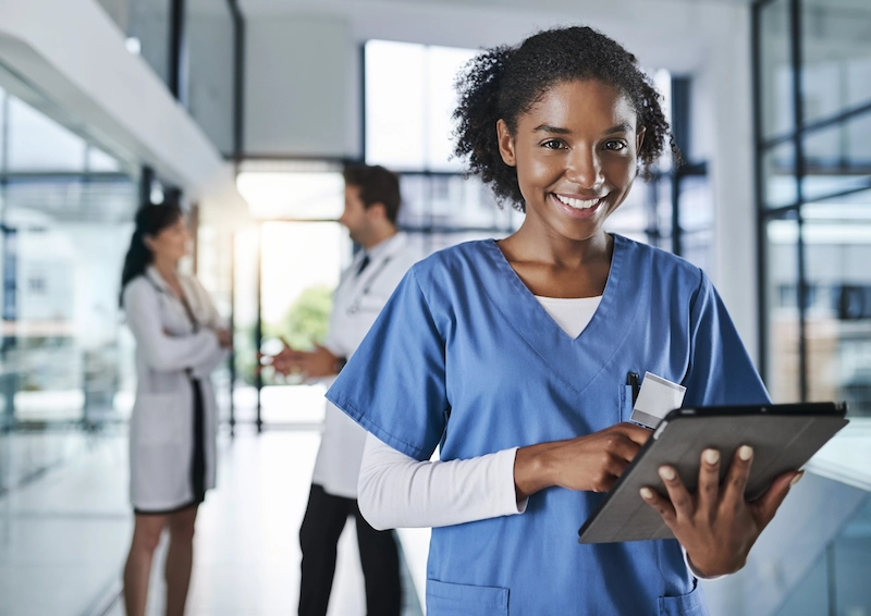 Smiling female clinician holding a tablet while walking down the hall of a medical facility.